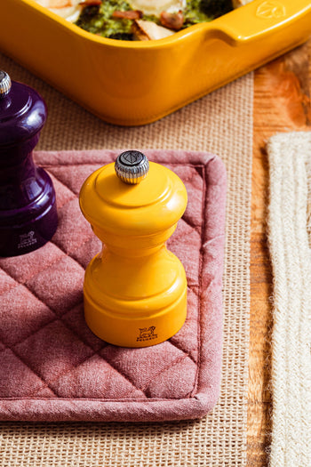 Salzmühle in safrangelb und Aubergine von Peugeot auf einem rosa Topflappen
